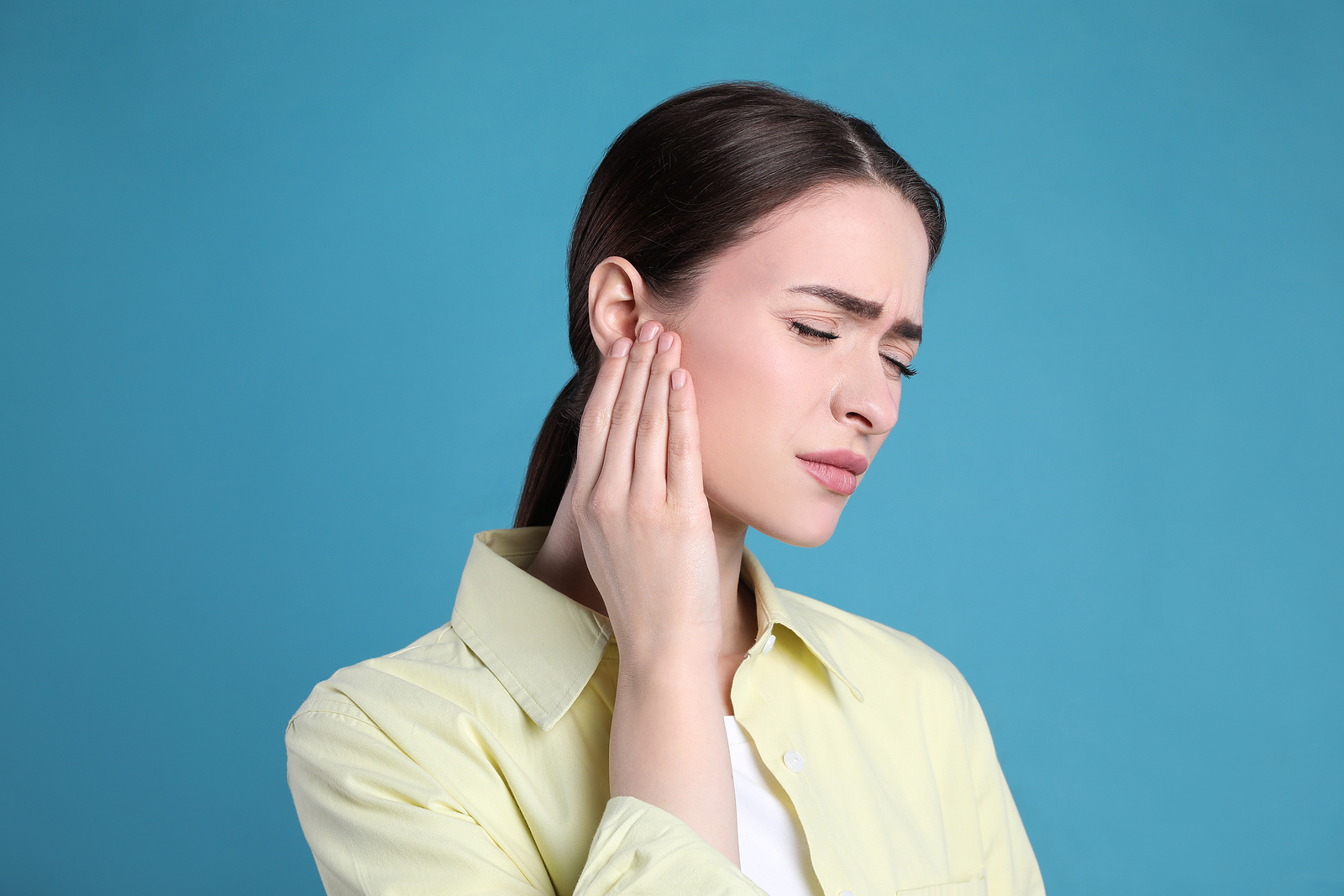 Young Woman Suffering From Ear Pain On Light Blue Background